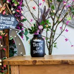 A small wooden table with a floral display and a bottle, which has the words 'Taste of India' painted on it.