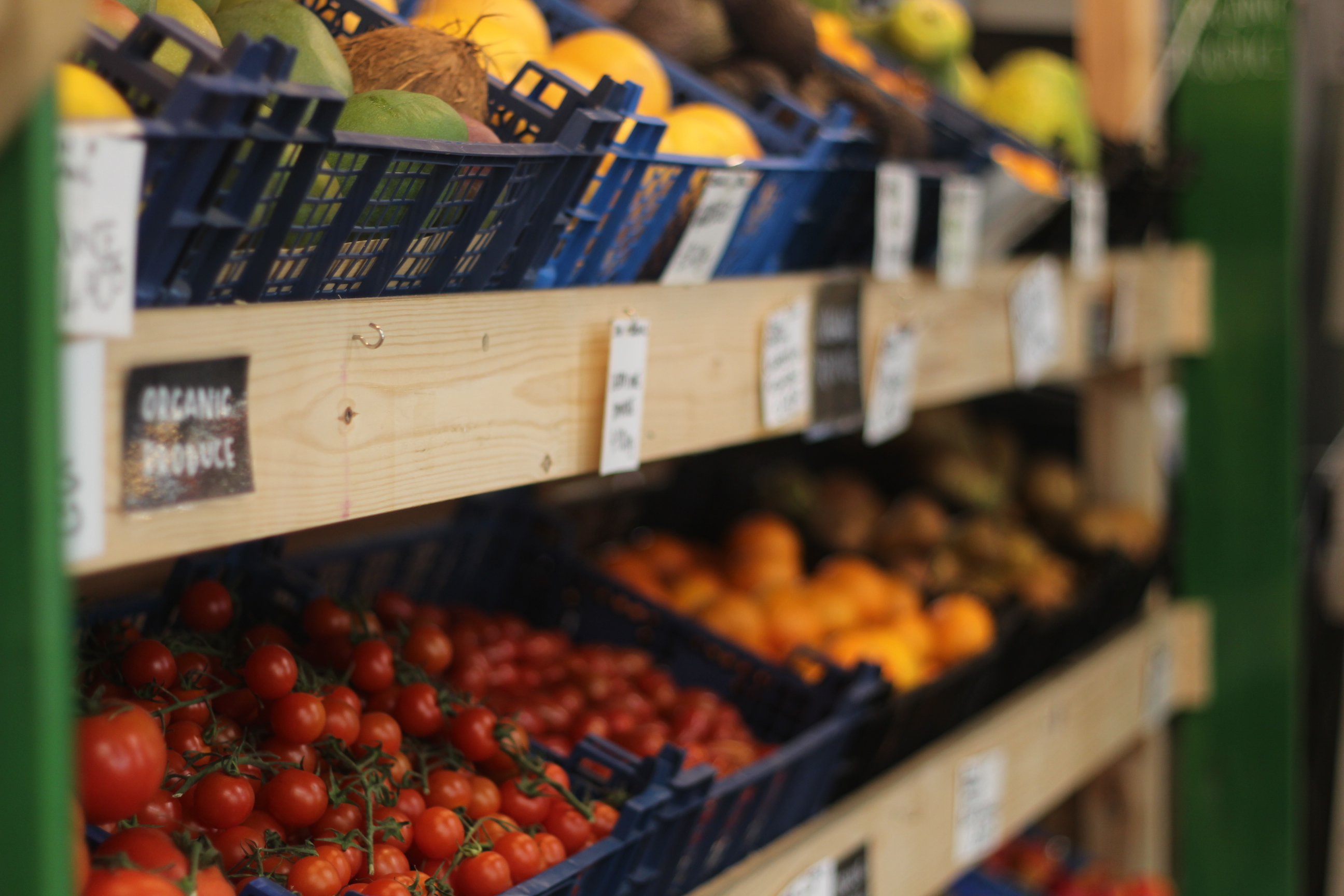 Wooden shelves with crates full of tomatoes, mangoes, coconuts and oranges.