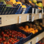 Wooden shelves with crates full of tomatoes, mangoes, coconuts and oranges.