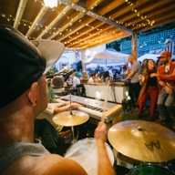 People gathered round, at dusk, listening to a band play in an outdoor setting.