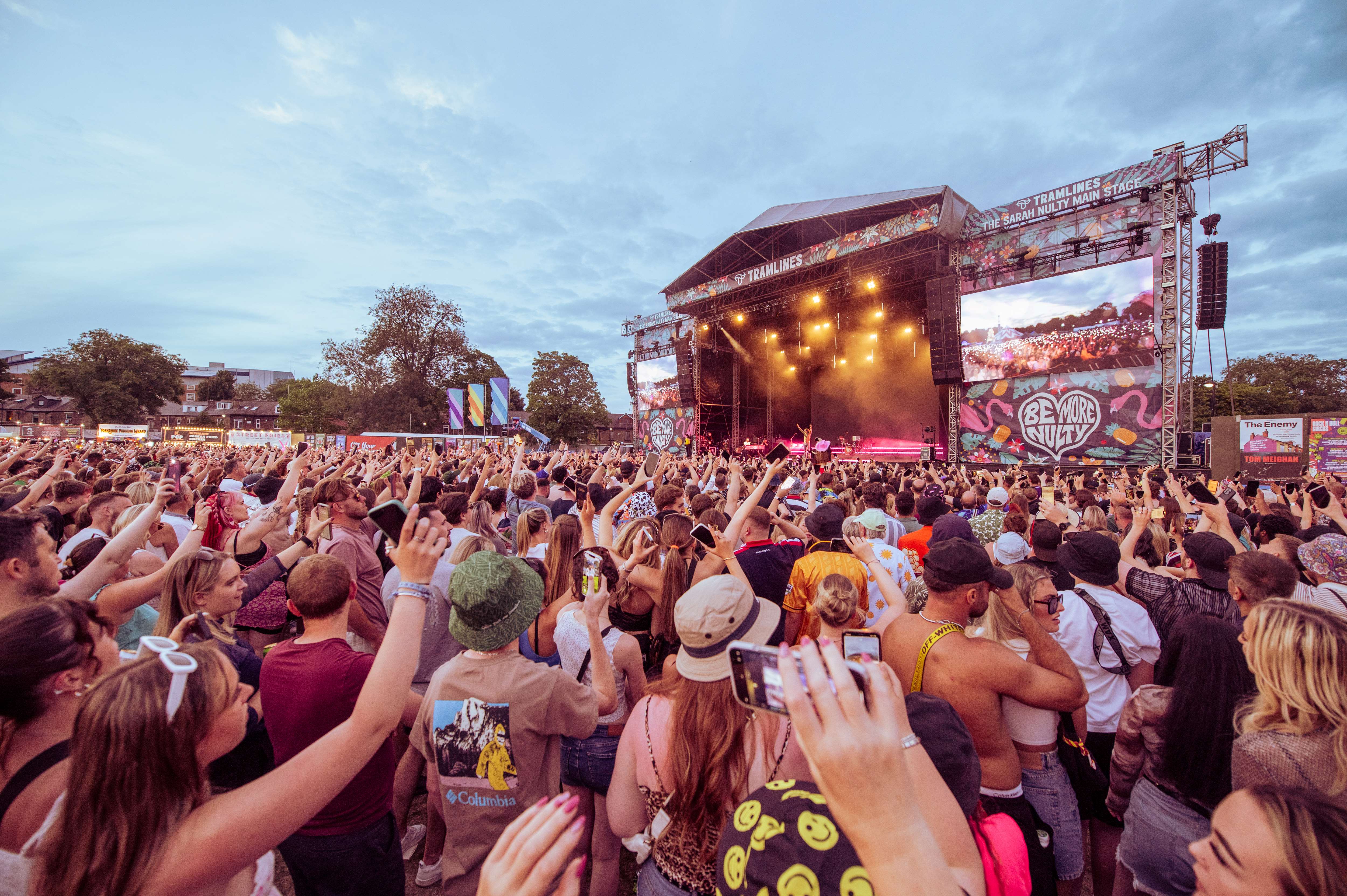 A crowd view looking looking towards the tramlines main stage from the right side as hundreds of people lift their arms in the air