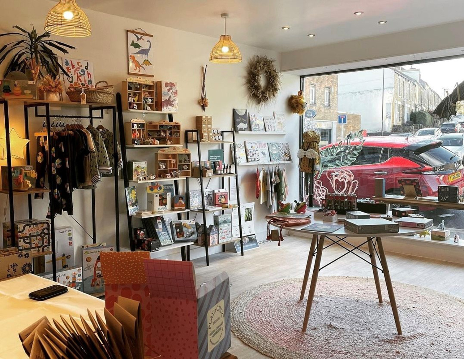 The interior of a small shop selling a variety of goods including clothes, greeting cards, pictures, plants and books.