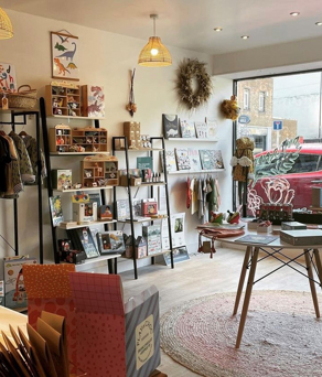 The interior of a small shop selling a variety of goods including clothes, greeting cards, pictures, plants and books.