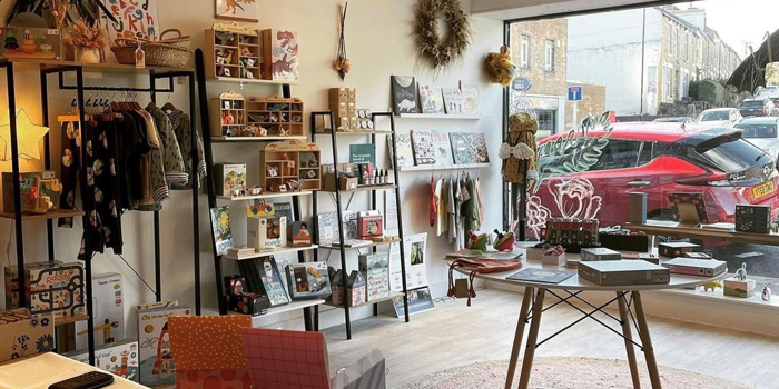 The interior of a small shop selling a variety of goods including clothes, greeting cards, pictures, plants and books.