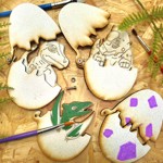 Three 2D wooden dinosaur eggs, that open to reveal a dinosaur, lie on a table ready to be decorated.