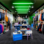Inside the Glass Onion shop. All the walls are full of clothes on rails. In the centre of the shop are tables with accessories on display.