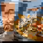 A drink and a bowl of nachos covered in melted cheese, sour cream and jalapenos.