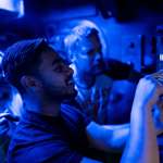 Three people in a room dimly lit by blue light are solving a puzzle at The Great Escape.