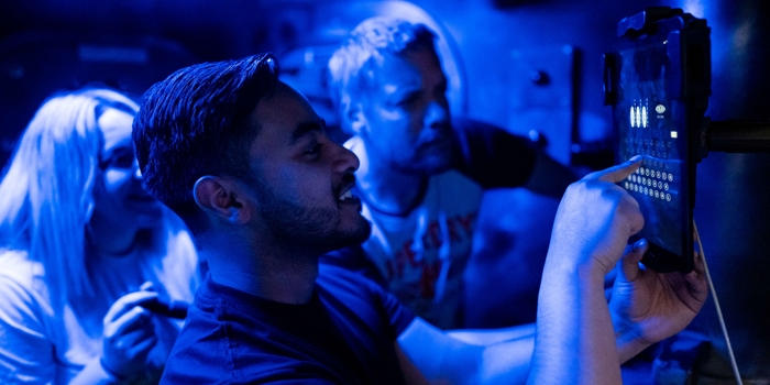 Three people in a room dimly lit by blue light are solving a puzzle at The Great Escape.