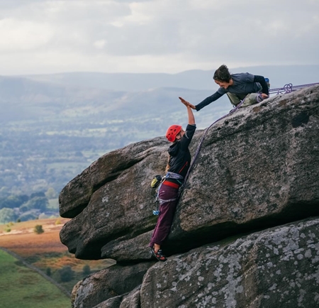 Two climbers on a rocky outcrop high-fiving each other.
