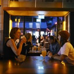 Two people drinking across the table from one another in Factory Floor 