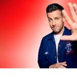 A promo shot of Chris Ramsey holding his hand up, towards the camera. 