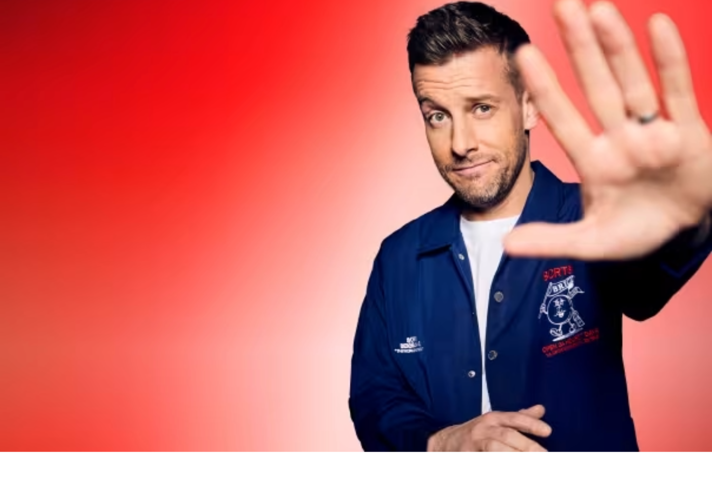 A promo shot of Chris Ramsey holding his hand up, towards the camera. 