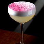 A yellow cocktails with a pink dusting on top.