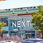 The NEXT store at Meadowhall with a large glass façade, prominent signage and surrounding trees and parked cars in the foreground.