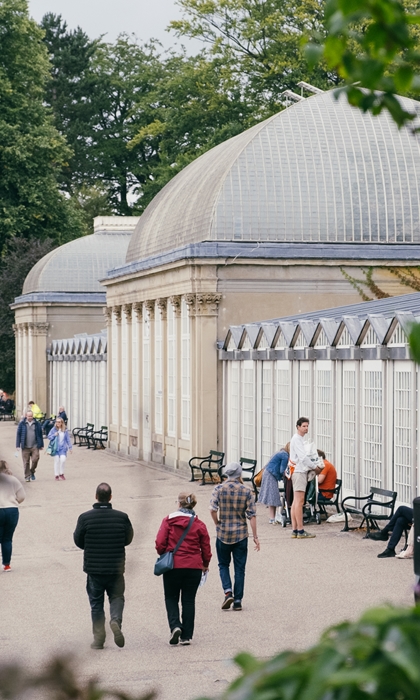 People are strolling along the wide path that runs along the length of the glass house in Sheffield Botanical Gardens.