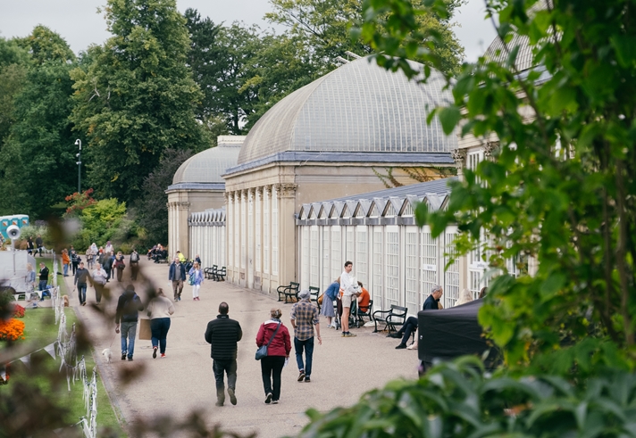 People are strolling along the wide path that runs along the length of the glass house in Sheffield Botanical Gardens.