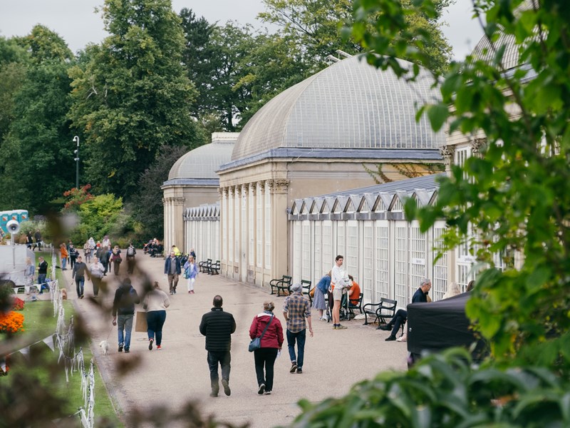 People are strolling along the wide path that runs along the length of the glass house in Sheffield Botanical Gardens.