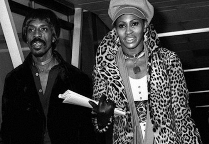 A black and white image of two people walking through a public space.