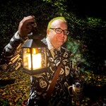 A man in a Halloween themed suit holding an old fashioned lantern.