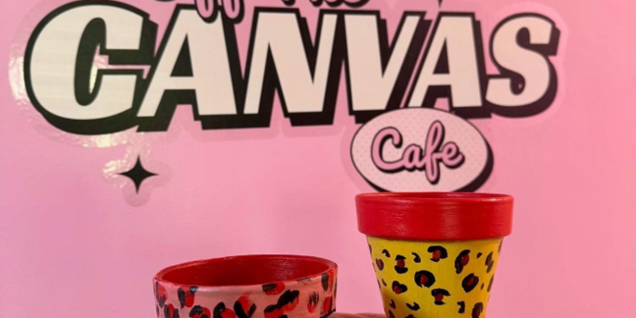 A hand is holding up a decorated pot in front of a  pink wall that has logo on it that reads 'OFF THE CANVAS'.
