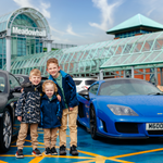 Three boys stand between 2 supercars in the Meadowhall carpark. 