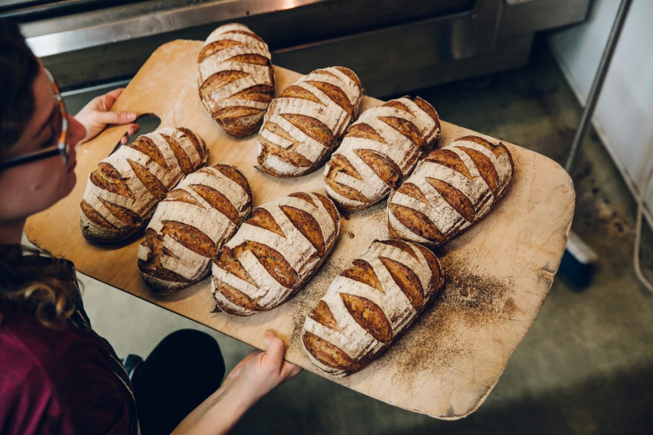 Eight loaves of bread being taken out of the oven.