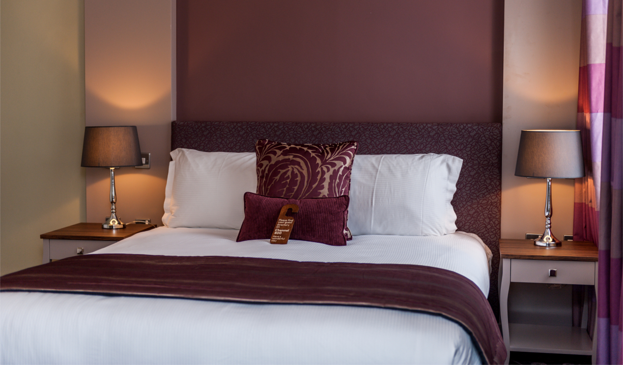 Elegant double bed with plush bedding and accent cushions in a cosy hotel room.