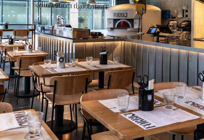 Inside Forbici, with tables and chairs throughout the restaurant and a wood fired pizza oven in the corner.