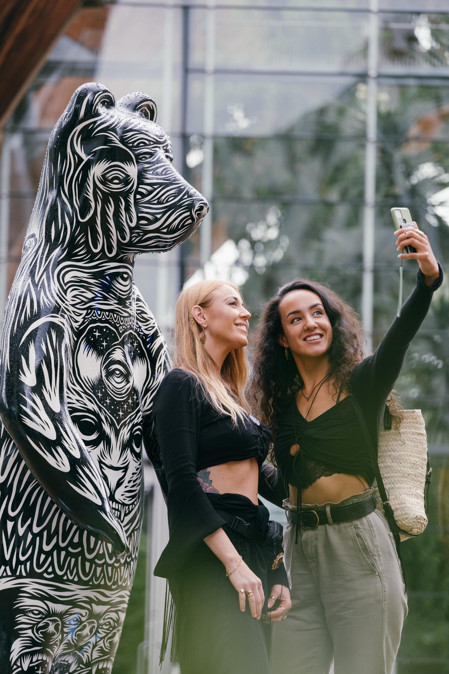 Two women taking a selfie in front of a statue of a bear that has been decorated by Sheffield artist Tom J Newell. The bear is one of The Bears of Sheffield which was a large public sculpture trail that span the city of Sheffield throughout the summer of 2021.