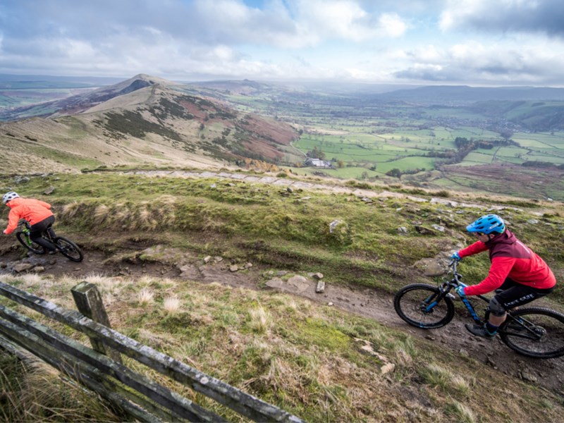 Two people mountain biking along a muddy track out in the countryside.