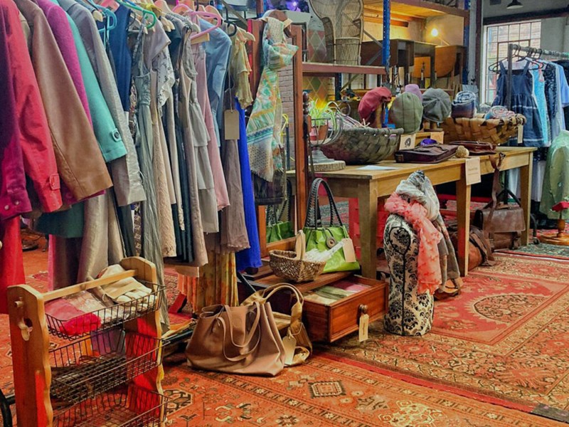 Inside The Warehouse with shelves and tables covered in things to buy and rails full of clothes.