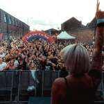 A performer on stage in front of a big crowd. In the middle of the audience is an arch with the words 'LOVE TO BE'.