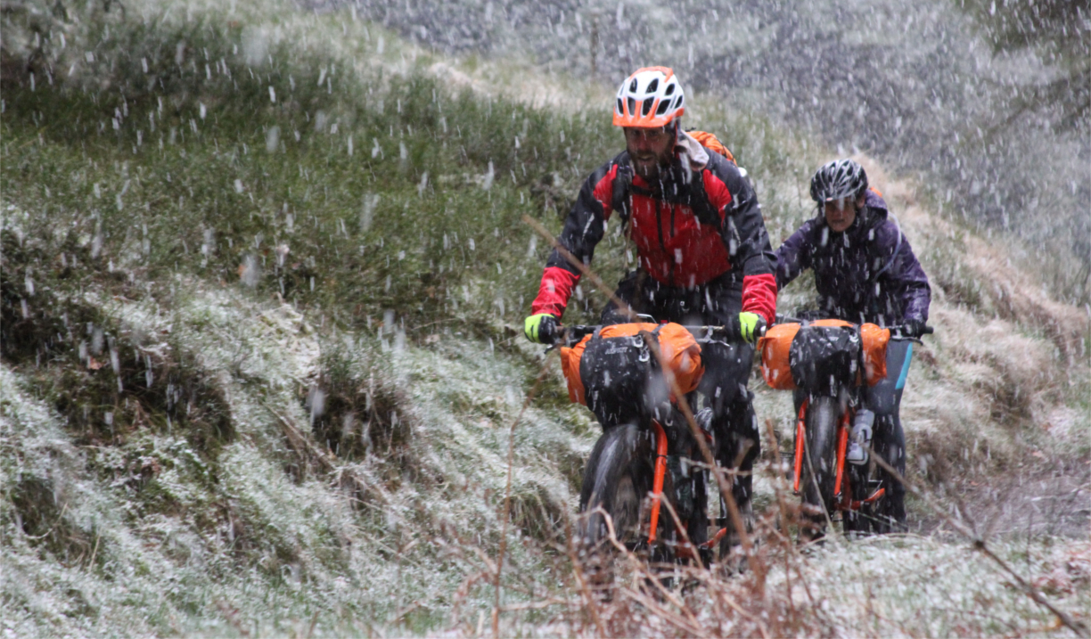 Two people cycling along a track in the countryside, in heavy rain.