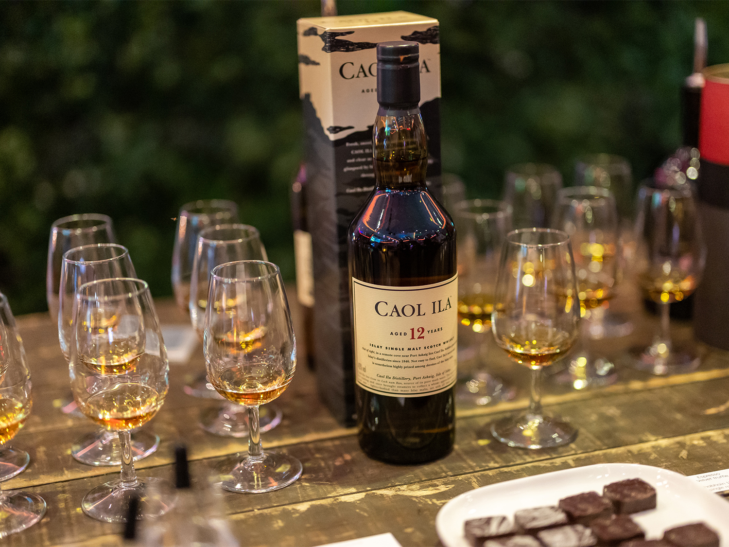 A bottle of single malt whisky is stood on a table surrounded by tasting glasses filled with a sample of the Whisky.