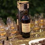 A bottle of single malt whisky is stood on a table surrounded by tasting glasses filled with a sample of the Whisky.