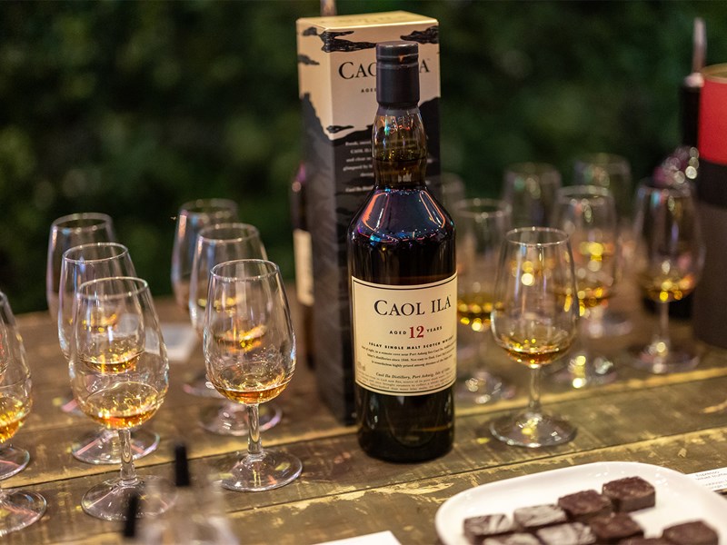 A bottle of single malt whisky is stood on a table surrounded by tasting glasses filled with a sample of the Whisky.