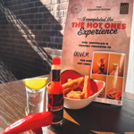 A table with a menu, a shot of spirits, a bottle of hot sauce and some red chillies. 