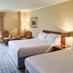 Bright, well-lit bedroom featuring two double beds with coordinated bedding and a cosy seating area near the window.