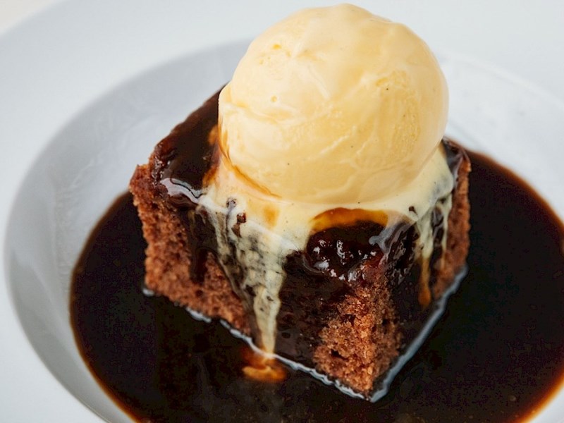 A cake covered in sauce with a scoop of ice cream on top.