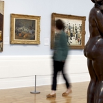 Inside Graves Gallery a woman is standing in front of three paintings.