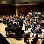 A full symphony orchestra playing on-stage in a concert hall.