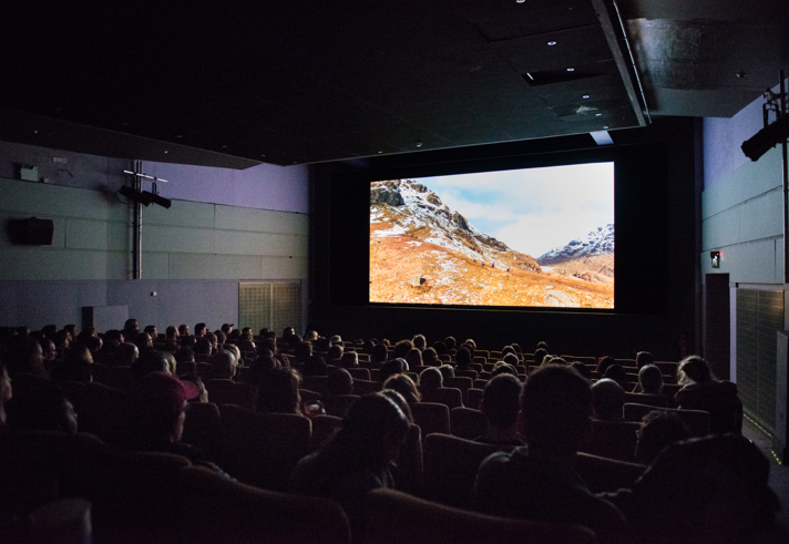 Cinema room full of people, with a cinema screen showing a snowy mountain