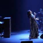 Imelda May performing live on stage in subdued blue lighting.