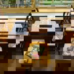 A table with two chairs and a stool, next to a window. There is a chess board on the table and a hard back book on the stool.