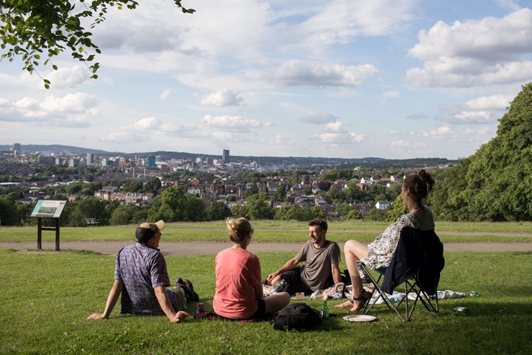 People enjoying the sun in Meersbrook Park with view of city beyond