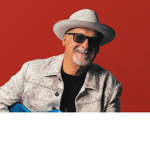A head-shot of the artist Paul Carrack against a red backdrop.