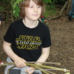 A child playing the woods. They have a headdress made of leaves and are carrying a bow and arrows made from sticks.