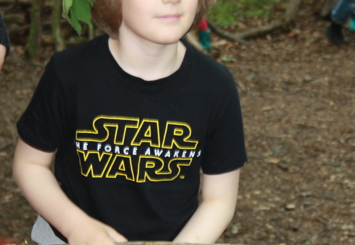 A child playing the woods. They have a headdress made of leaves and are carrying a bow and arrows made from sticks.