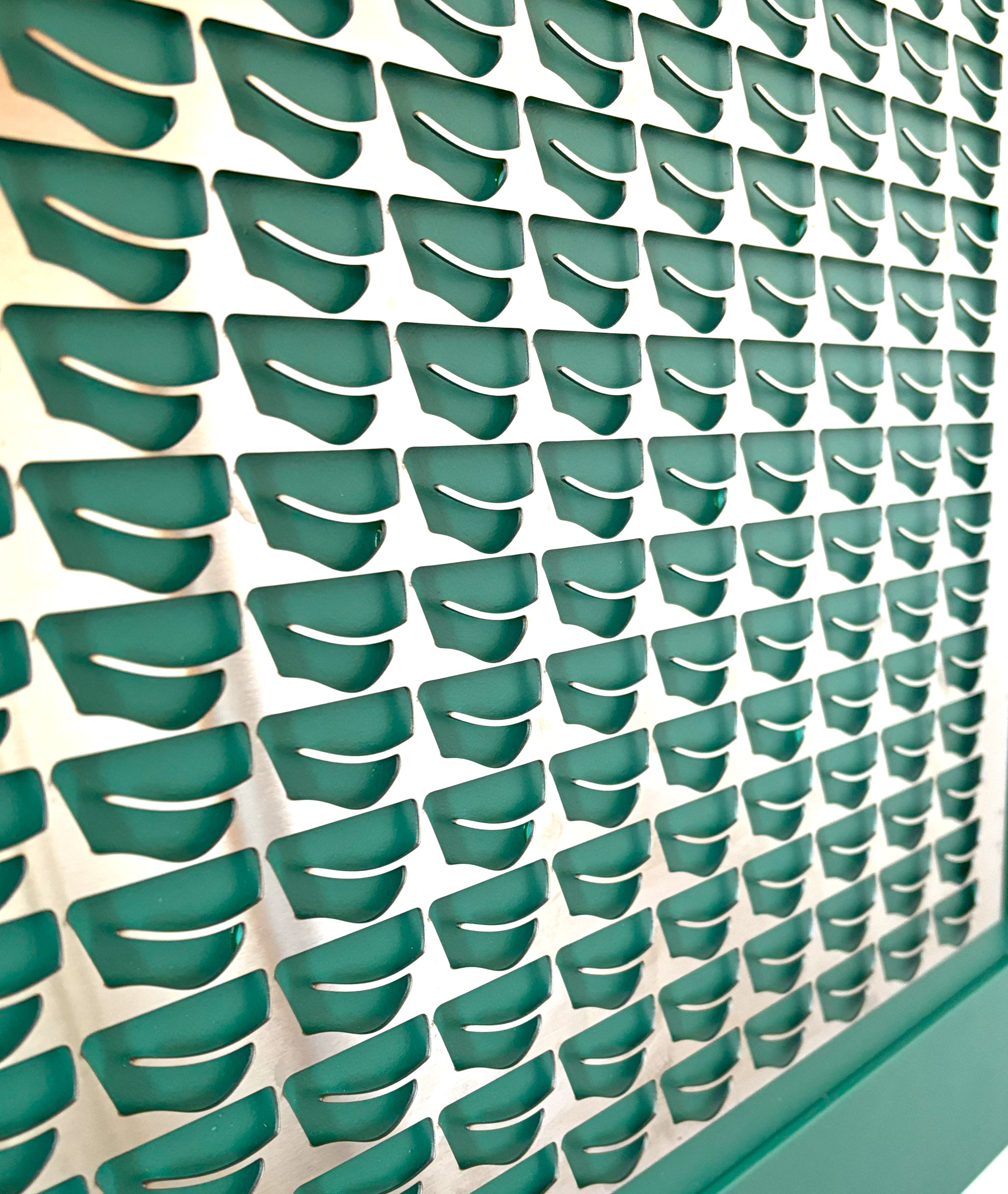 Close-up of a blue decorative panel with a silver metallic overlay featuring elongated spoon-like cut-out shapes arranged in a symmetrical pattern.